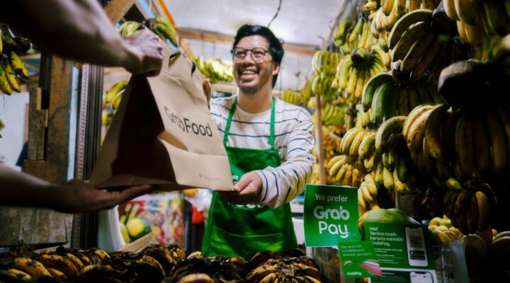 a man holding a paper bag in front of a bunch of bananas
