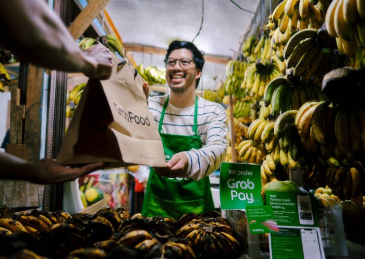 a man holding a paper bag in front of a bunch of bananas